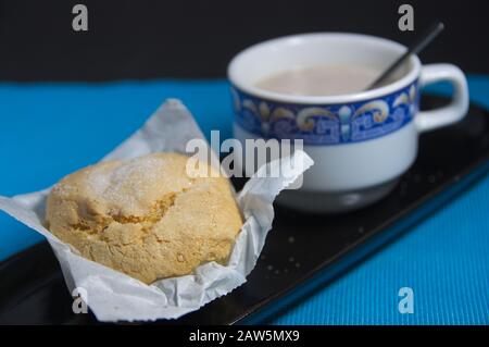 Tasse de cacao avec du lait avec un cupcake accompagnant servi tous dans un plateau en céramique noire sur une table bleue et fond noir Banque D'Images