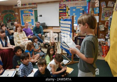 Étudiant de deuxième année à la Barton Hills Elementary School d'Austin, Texas lit son rapport scientifique aux camarades de classe lors d'une « fête d'édition » pour les sujets scientifiques, tandis que les parents écoutent à l'arrière de la chambre. Banque D'Images