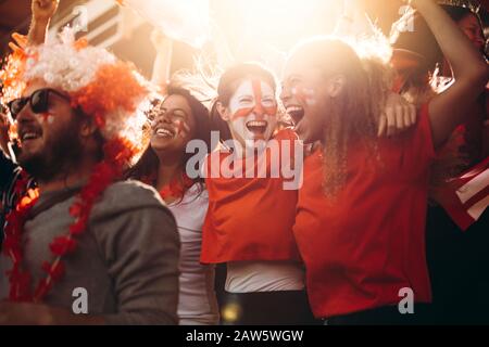 Les supporters de football de l'Angleterre applaudissants dans les tribunes. Les femmes avec drapeau d'Angleterre peint sur leurs visages s'amuser dans la zone de ventilateur au stade. Banque D'Images