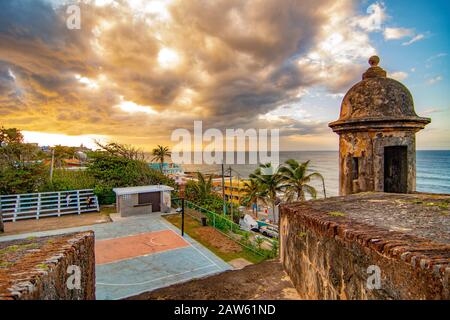 Une tour d'observation au fort Castillo San Cristobal surplombe les maisons colorées de la Perla et un terrain de basket-ball avec un coucher de soleil coloré. Banque D'Images