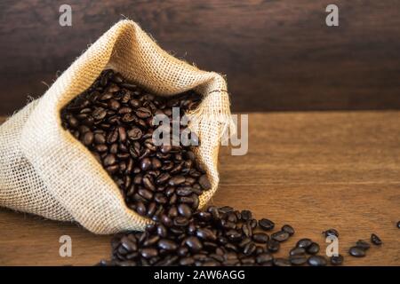 Grains de café rôtis déversés du sac de jute sur des planches en bois Banque D'Images