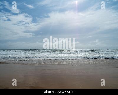 Vagues se déroulant sur la rive et le soleil qui brillent à travers les nuages, sable humide étincelant, plage australienne Banque D'Images