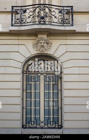 Une pierre mascaron masque la pierre de touche au-dessus d'une fenêtre voûtée sous un balcon juliette avec des œuvres décoratives sur l'avenue Charles Floquet, Paris, France. Banque D'Images