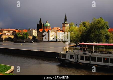 Prague, regardant le pont Charles, les dômes et les tours, à Kampa un bateau se déplace à travers le canal de Smíchov, avec des nuages sombres dramatiques et une lumière de tempête brillante Banque D'Images