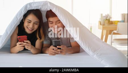 Les amoureux des couples asiatiques qui mentent sur leur téléphone mobile de jeu sur le lit Banque D'Images