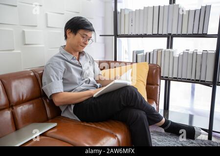 Livre de lecture de l'homme asiatique senior sur le canapé dans le salon à la maison, Portrait de l'homme asiatique âgé est Relaxant et bonheur Avec Read a Magazine Banque D'Images