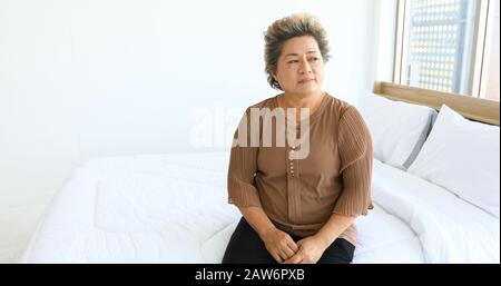 Une femme âgée assise seule sur le lit Banque D'Images