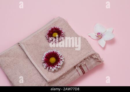 Serviette éponge douce avec gerbera rouge et boutons de fleur d'orchidée blanc sur fond rose. Vue de dessus. Banque D'Images