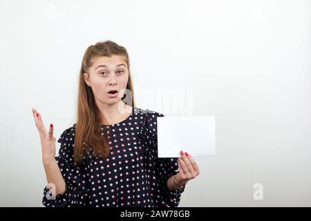 Une fille à poil équitable en robe noire avec des cercles blancs montre du papier blanc à la surprise Banque D'Images