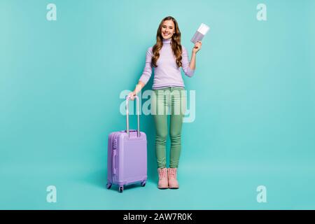 Photo pleine longueur de l'aéroport de jolie dame documents d'enregistrement des billets de voyage roulant valise porter lilas pullover vert pantalon chaussures Banque D'Images