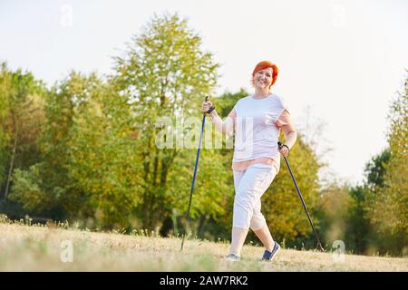 Heureuse femme faisant de la marche nordique en été dans le parc Banque D'Images