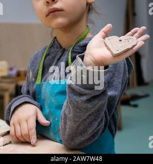 Une fille de 6 ans montre son artisanat d'argile - un coeur comme cadeau à la mère, maître de classe dans un atelier de poterie Banque D'Images