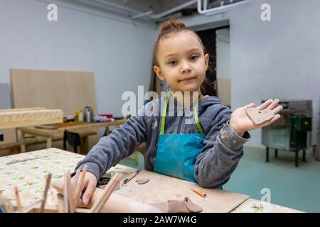 Une fille de 6 ans montre son artisanat d'argile - un coeur comme cadeau à la mère, maître de classe dans un atelier de poterie Banque D'Images