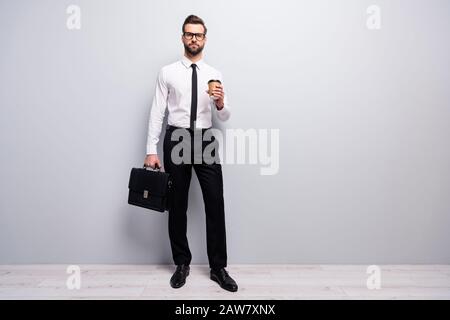 Photo pleine longueur confiante cool agent élégant marketer homme tenir mug Latte boisson porter cuir sac à main besoin de démarrage conférence porter blanc noir Banque D'Images