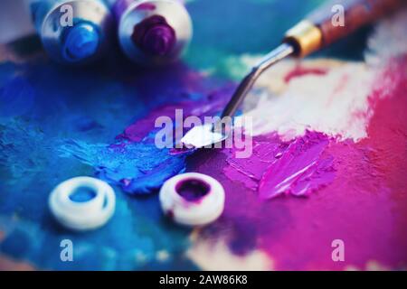 Sur la palette, tachée de peinture, il y a des tubes de peinture bleu vif et violet et un couteau à palette. Le couteau à palette frotte la couleur ultramine. Banque D'Images