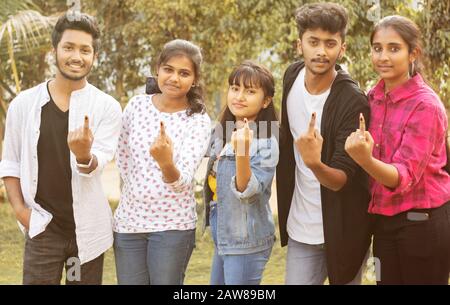 Groupe d'amis adolescents montrant des doigts marqués à l'encre devant le bureau de vote ou le stand après avoir exprimé des votes - concept de l'élection ou de la diffusion des votes indiens Banque D'Images