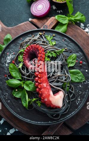 Pâtes noires avec tentacules de poulpe. Fruits de mer sur une assiette en pierre. Dans l'ancien arrière-plan. Vue de dessus. Espace de copie disponible. Banque D'Images