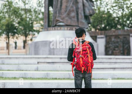 Un jeune photographe asiatique masculin avec un sac à dos brillant sur ses épaules photographie le monument. Vue arrière Banque D'Images