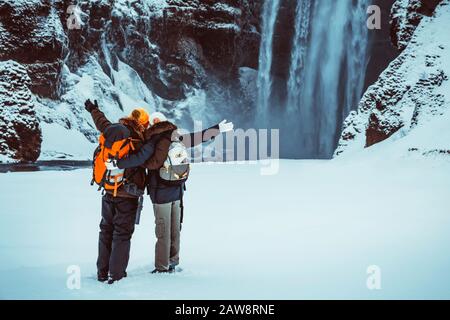 Joyeux couple profitant d'une vue imprenable sur la cascade de Skogafoss, s'amuser en hiver en Islande, lune de miel active en hiver Banque D'Images