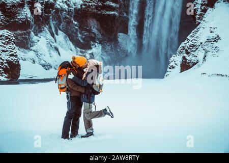 Jeune famille en vacances, voyageurs avec plaisir passer une lune de miel en Islande, baiser près de la chute d'eau de Skogafoss, couple heureux en vacances d'hiver Banque D'Images