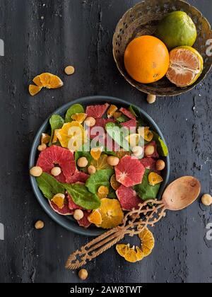 Vue de dessus de salade d'agrumes, avec feuilles d'épinards et noisettes dans un plat noir avec une cuillère en bois. Mélange de fruits tropicaux, cuisine, café Banque D'Images