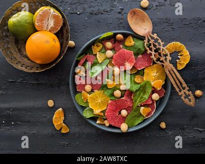 Vue de dessus de salade d'agrumes, avec feuilles d'épinards et noisettes dans un plat noir avec une cuillère en bois. Mélange de fruits tropicaux, citron vert, café Banque D'Images