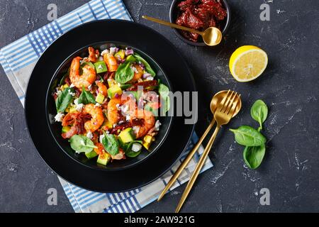 vue en hauteur de la salade d'épinards aux crevettes avec tomates séchées, morceaux de bacon frits, fromage émietté, oignon rouge dans un bol noir sur un t en béton Banque D'Images