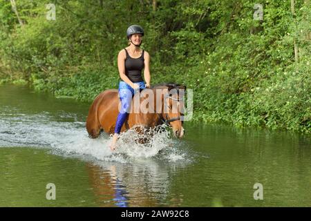Une jeune femme qui monte sur une base de poney dans un ruisseau Banque D'Images