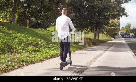 Jeune homme d'affaires décontracté qui monte en scooter électrique sur un trottoir en été Banque D'Images