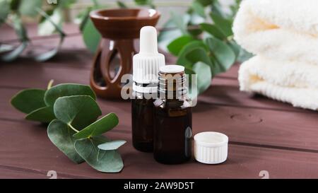 bouteilles avec de l'huile essentielle et feuilles d'eucalyptus sur une table en bois contre le fond d'aromalampes et de poulets Banque D'Images