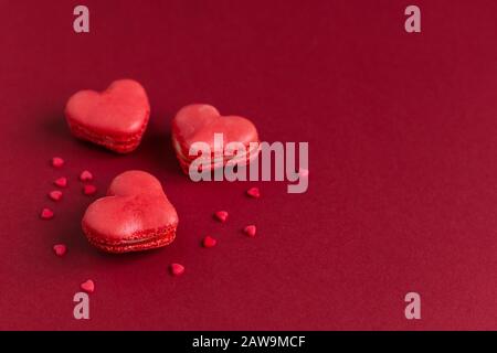 Macarons en forme de coeur sur un fond rouge foncé, décorés de coeurs doux. Concept pour la Saint Valentin. Placer pour le texte. Banque D'Images