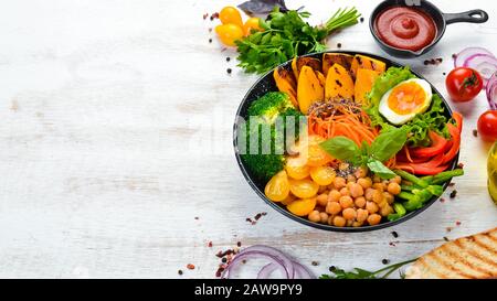 Bol de Bouddha : citrouille, brocoli, oeuf, tomates, carottes, paprika dans une plaque noire sur fond de bois blanc. Vue de dessus. Espace libre pour votre texte. Banque D'Images