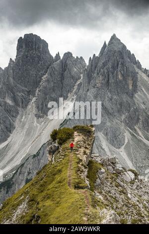 Homme avec veste rouge debout sur un degré, derrière lui des pics de montagne et des roches pointues, des nuages dramatiques, Cimon le groupe Croda Liscia et Cadini Banque D'Images