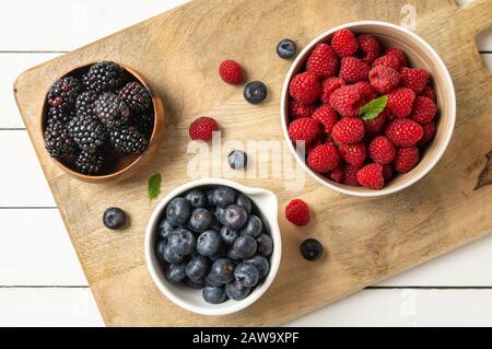 trois bols aux baies sauvages, framboises, bleuets, mûres, sur fond rustique en bois Banque D'Images