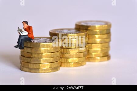 Modèle de jeune homme lisant un journal et regardant pensif tout en assis sur une pile de monnaie d'une livre. Banque D'Images