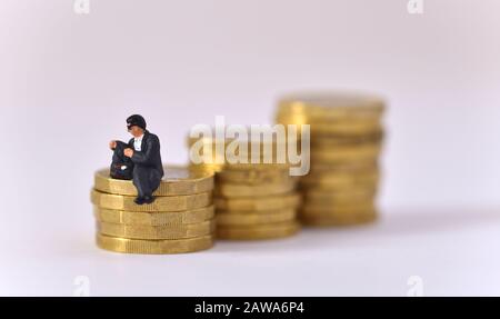 Modèle d'homme portant des lunettes de soleil et regardant dans la poche de veste tout en étant assis sur une pile de monnaie d'une livre. Banque D'Images