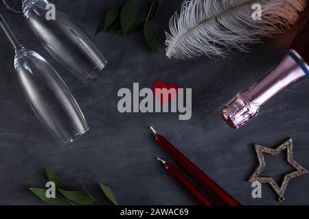 Composition plat avec bouteille de champagne, bougies, plumes et coeurs pour la célébration sur fond de béton gris. Verre de champagne Banque D'Images