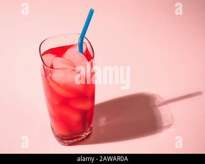 gros plan de verre de poinçon de fruits rouges avec des glaçons et de la paille bleue jetant une ombre sur fond rose Banque D'Images