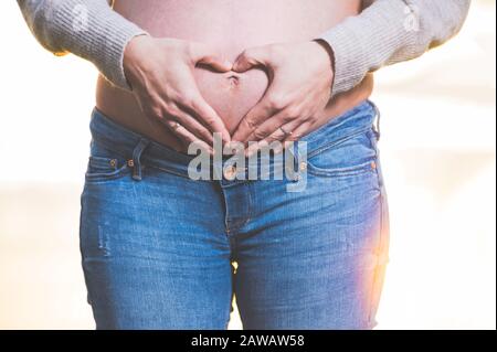 Les mains de la femme enceinte qui font de la forme de coeur sur le ventre . Banque D'Images