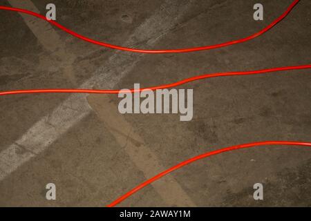 Câble d'alimentation électrique rouge. Le fil rouge se trouve au sol. Mess sur le sol en ciment. Arrière-plan industriel Banque D'Images