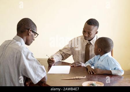 Père africain avec son fils s'appliquant à l'école avec le directeur de l'école en signant un contrat dans un bureau Banque D'Images