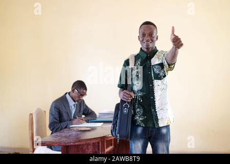Jeune et heureux collègue africain d'affaires montrant son pouce pour exprimer le bonheur et le sourire gai isolé sur le fond Banque D'Images