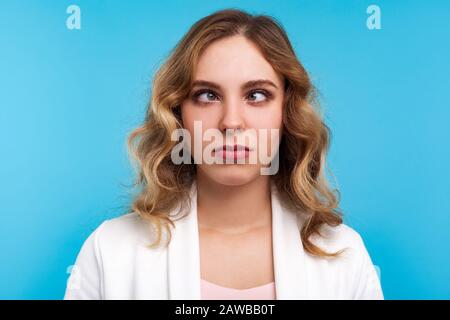 Gros plan portrait d'adorable femme drôle avec des cheveux ondulés dans la veste blanche regardant la croix avec l'expression ridicule maladroite du visage, calmant les yeux Banque D'Images