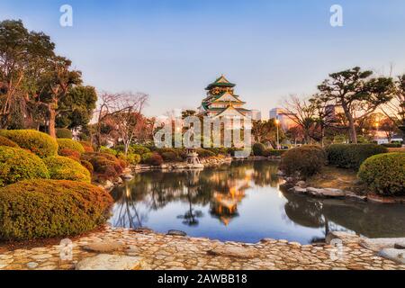 Petit étang encore au milieu du parc public et du quartier historique de la ville d'Osaka au lever du soleil. Reflet des pins verts et de la tour du château du patrimoine. Banque D'Images