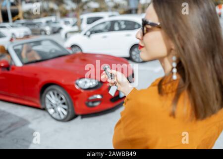 Jeune femme tenant la trousseau d'une voiture rouge neuve achetée ou louée sur le parking extérieur Banque D'Images