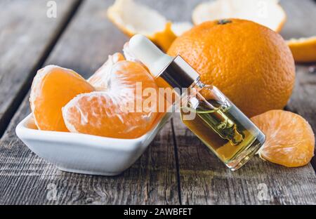 Huile essentielle de mandarine dans une bouteille de verre près d'un bol blanc avec des tranches de mandarine. Agrumes, mandarines ou oranges. Médecine alternative Banque D'Images