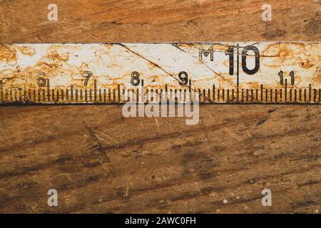 Ancienne règle rouillée avec numéros noirs sur une table en bois en état de marche. Ruban de mesure vintage. Arrière-plan industriel. Atelier de menuiserie avec espace de copie Banque D'Images