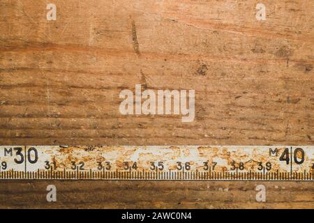 Ancienne règle rouillée avec numéros noirs sur une table en bois en état de marche. Ruban de mesure vintage. Arrière-plan industriel. Atelier de menuiserie avec espace de copie Banque D'Images