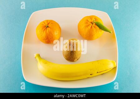 Tangerines kiwi et une banane sur une plaque blanche organisée comme un visage humain souriant Banque D'Images