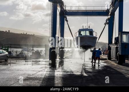 Nettoyage de la coque inférieure d'un bateau suspendu dans une grue de levage dans un quai sec au port de Playa San Juan, Tenerife, îles Canaries, Espagne Banque D'Images